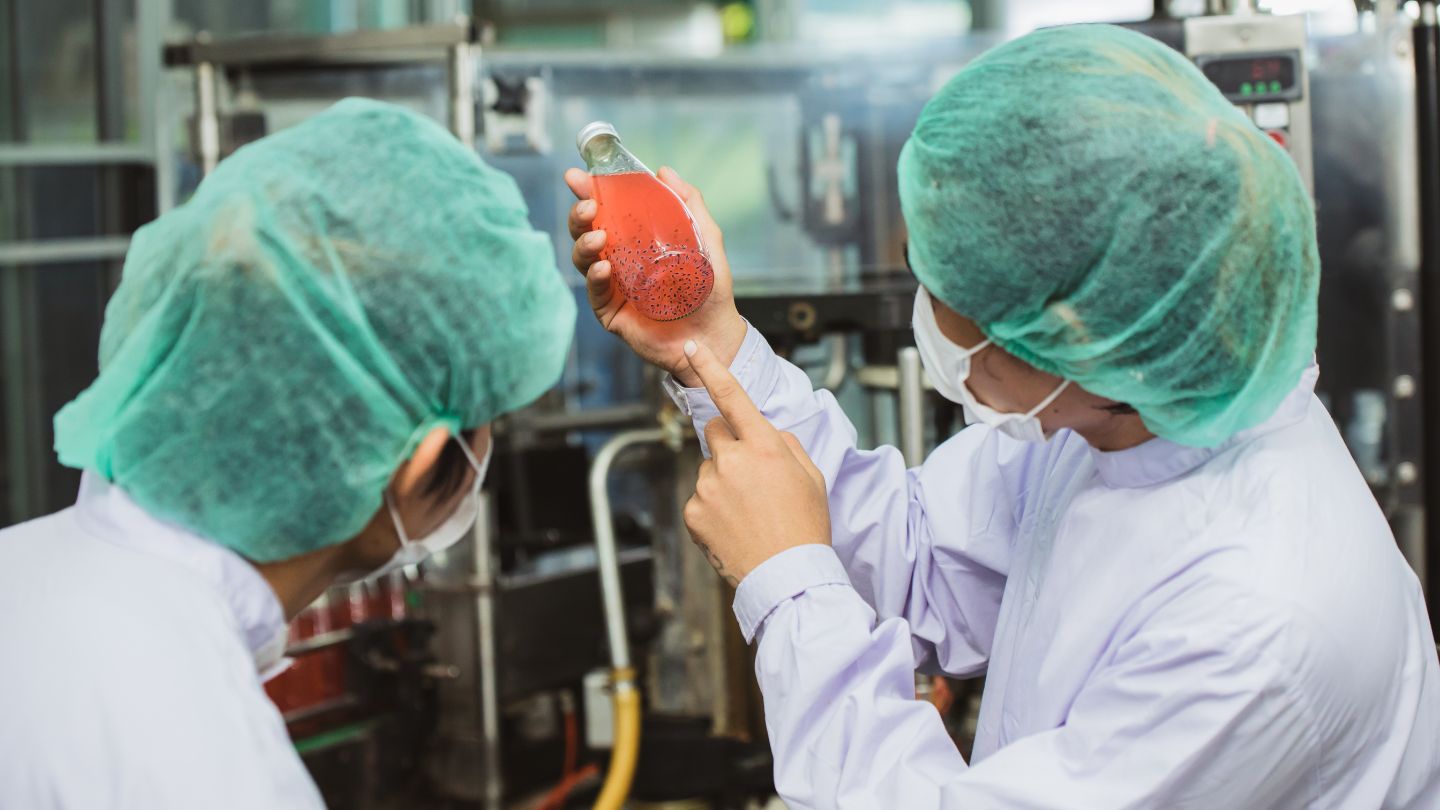 Two masked food safety workers inspect manufactured beverages to ensure FDA compliance and safeguard against these common FDA violations examples.
